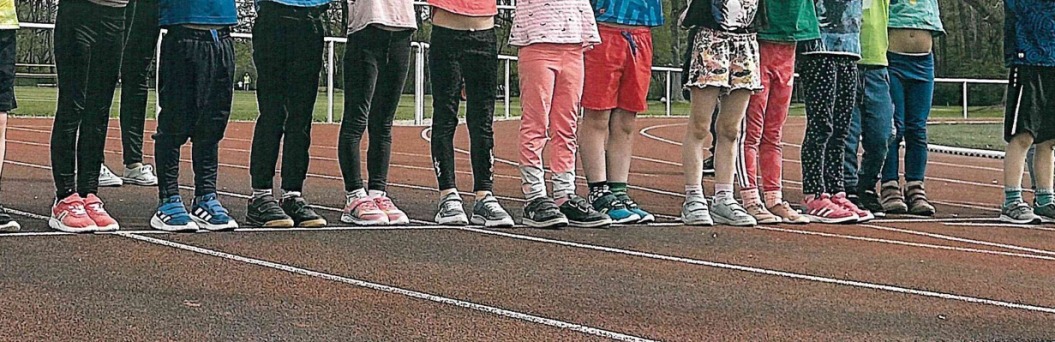 Zu sehen sind Kinderbeine und Füße am Start einer roten Crosslaufstrecke.
