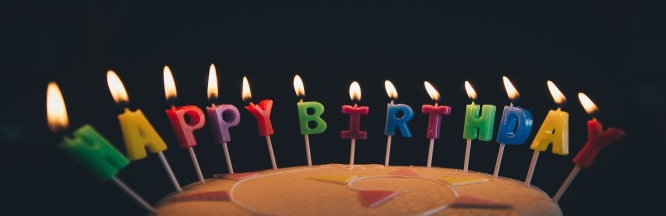 bunte Torte mit brennenden Kerzen und Schriftzug Happy Birthday