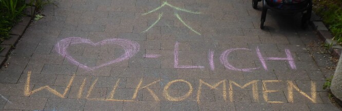 Auf Asphalt steht mit bunten Kreidebuchstaben "Herzliche Willkommen" geschrieben