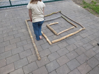 aus unterschiedlich langen holzstangen wurde eine Spiralform gelegt. Ein Kind lbalanciert zwischen den Stangen hindurch. 