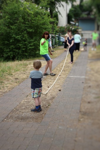 Eine erwachsene Person und ein Kind ziehen an unterschiedlichen Seilenden an einem langen Seil. 