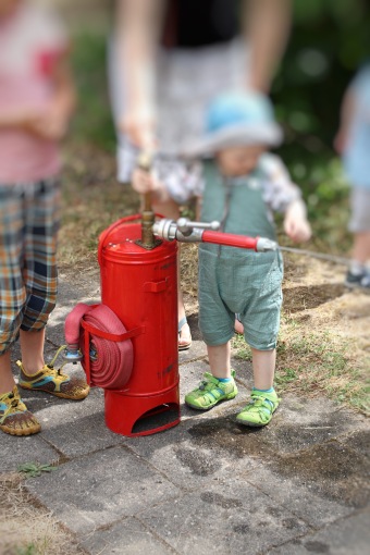 Ein Kleinkind bedient eine Rote Wasserpumpe 
