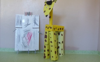 Aus Pappen und Kartons wurde eine große gelbe Giraffe gebaut. Daneben steht ein einfacher Roboter aus Pappe und Wäscheklammern.