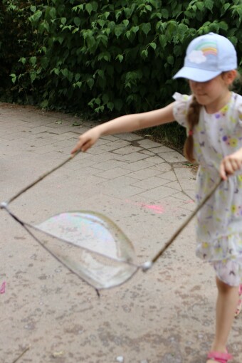 Ein Mädchen macht eine Riesenseifenblase mit einer an Stöckern befestigten Schnur.