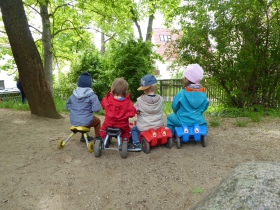 Es sind 4 Kinder von hinten auf ihren Rutschautos sitzen.