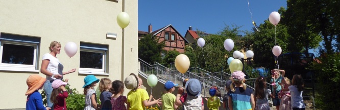 Erzieherin und Kinder halten Luftballons in den Himmel