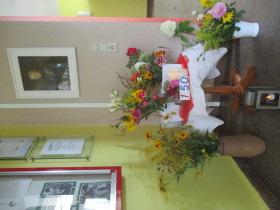 Ein Bild Maria Montessoris an der Wand und darunter Blumen in einer Vase. 