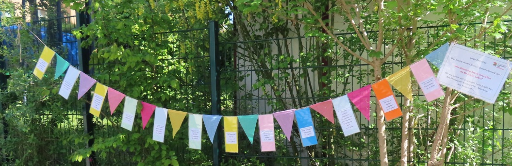 bunte Wimpelketten hängen am Gartenzaun. Daran befestigt sind Zettel mit Kindersprüchen. 