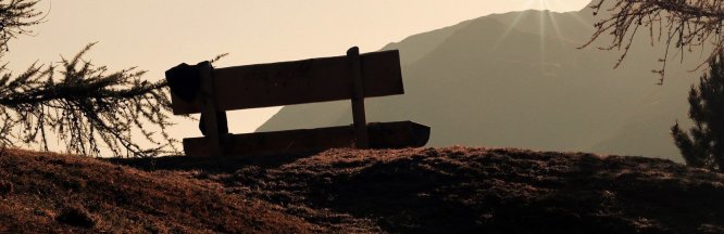 Eine Holzbank steht bei Sonnenuntergang auf einem Berg