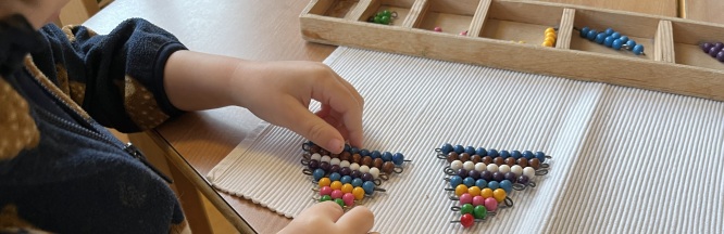 Zu sehen sind Kinderhände, welche über einer Montessoriübung namens bunte Perlenstäbschen gehalten werden.
