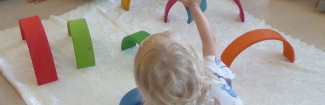 Ein Kind spielt auf dem Teppichboden mit bunten Holzbögen